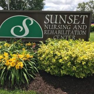 Signage of Sunset Nursing and Rehabilitation Center surrounded by vibrant flowers.