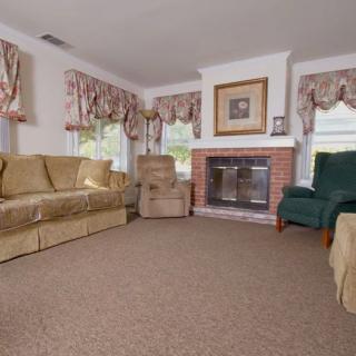 A cozy living room featuring a comfortable sofa, armchair, and a fireplace with decorative drapes framing the windows.
