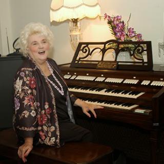 A smiling woman poses by an organ, showcasing a joyful moment in a warm, vintage setting.