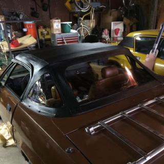 A vintage brown car with a convertible roof parked inside a cluttered garage.