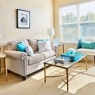 A bright and cozy living room with a beige sofa, colorful cushions, and a glass coffee table.