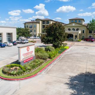 A hotel building with a landscaped entrance and parking lot under a blue sky with clouds.