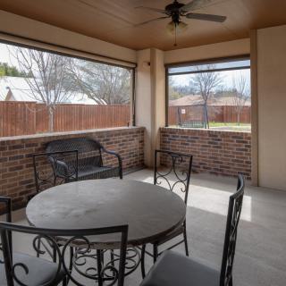 A cozy screened patio with a round table and metal chairs, surrounded by brick walls and overlooking a fenced yard.