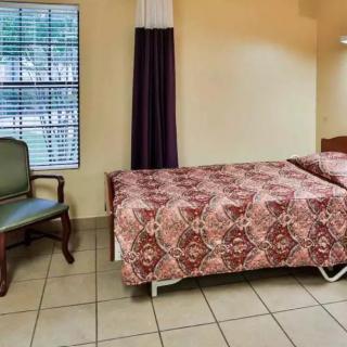 A simple hotel room with a bed, chair, and window covered by curtains.