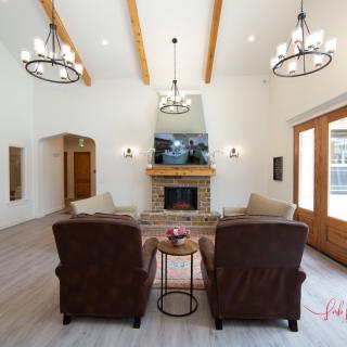 A spacious living room with a cozy fireplace, featuring wooden beams and elegant chandeliers.