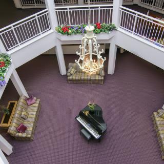 A view of a spacious lobby with a grand piano and chandelier, surrounded by seating areas on two levels.