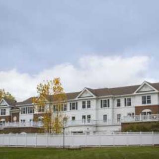 A suburban residential building with a white fence and trees under an overcast sky.