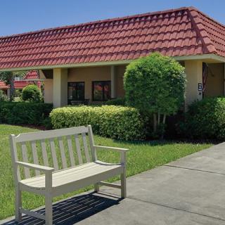 A quiet outdoor scene with a bench beside a sidewalk in front of a building with a red-tiled roof.