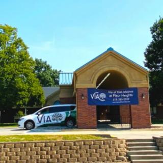 A vehicle parked in front of a community center with a banner displaying 'VIA' and promotional text.