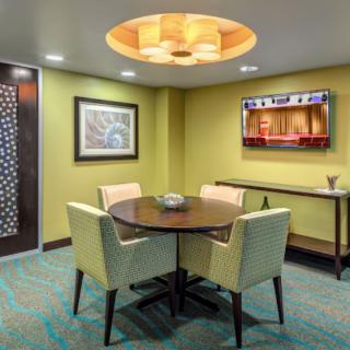 A cozy dining area with a round table, four chairs, modern lighting, and a television on the wall.