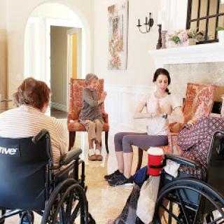 A caregiver engages with elderly individuals in wheelchairs during a group activity at a community center.