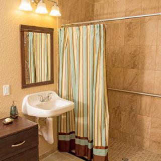 A cozy bathroom featuring a striped shower curtain, wall-mounted sink, and mirror with warm lighting.