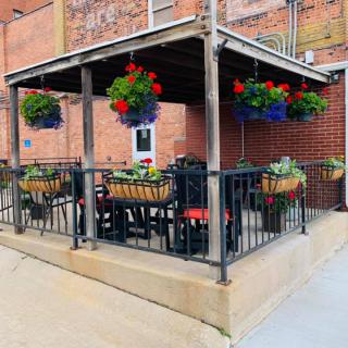 An outdoor patio area with tables and chairs, decorated with hanging plants and located next to a brick building.