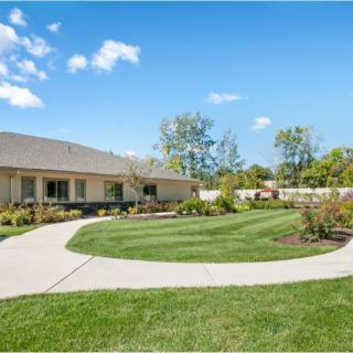 A beautiful house with a well-maintained lawn and garden, featuring a curved driveway under a clear blue sky.