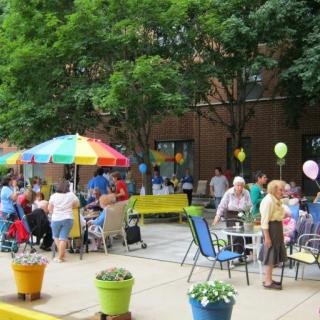 A lively outdoor event with people socializing under colorful umbrellas and balloons.