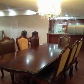 Elegant dining area with a polished wooden table, ornate chairs, and a chandelier, adjacent to a modern kitchen.