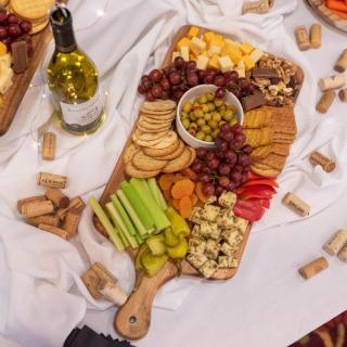 A beautifully arranged cheese and charcuterie board with an assortment of snacks, accompanied by a bottle of wine.