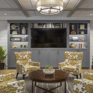 A cozy living room with floral chairs and a large television, surrounded by shelves filled with decor.