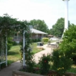 A serene garden with a pathway, lush greenery, and an archway leading to a building.