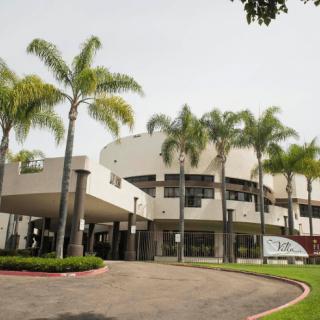 A modern building with a circular design, surrounded by palm trees and featuring a well-maintained driveway.
