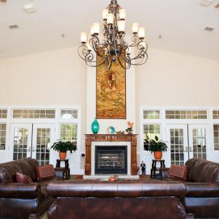 A spacious living room featuring a central fireplace, elegant chandelier, and leather sofas.