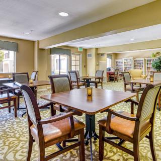 A bright and spacious dining area with tables and chairs, featuring large windows and a carpeted floor.