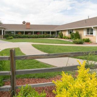 A building with a landscaped garden, featuring a wooden fence, pathway, and green lawn under a partly cloudy sky.