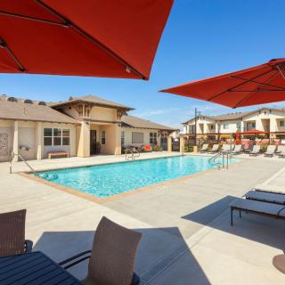 A sunny day by the pool in a residential area with lounge chairs and umbrellas.