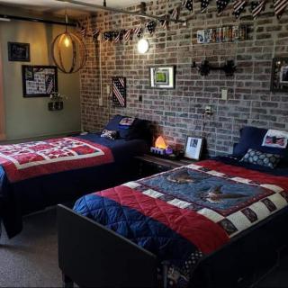 A cozy bedroom with twin beds covered in colorful quilts, decorated walls, and a brick backdrop.