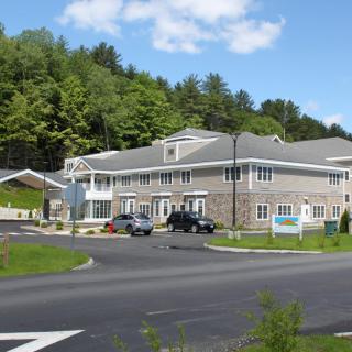 A modern office building with a parking lot and surrounding greenery under a clear blue sky.