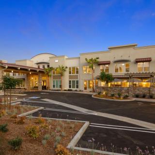 A modern residential building with a well-lit exterior in the evening, featuring a spacious parking area.