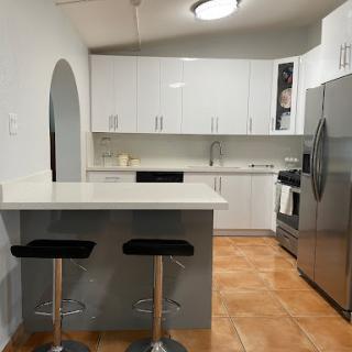 A modern and minimalist kitchen featuring sleek white cabinets and stainless steel appliances, complemented by stylish bar stools.
