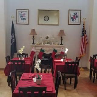 A cozy restaurant dining area with red tablecloths, neatly arranged tables and chairs, decorative lamps, and American flags.