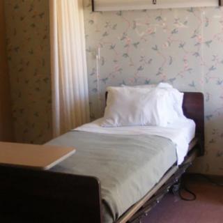 A hospital room with a single bed, pillow, and curtain.
