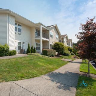 A suburban apartment building with landscaped surroundings and a sidewalk.