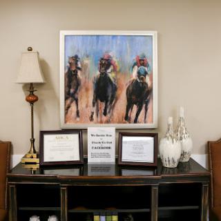 A decorated interior space featuring a painting of horses, accompanied by certificates and a lamp.
