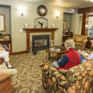 A group of seniors sitting in a cozy living room, engaged in conversation near a fireplace.