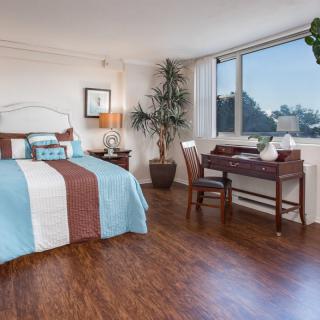 A well-decorated bedroom with wooden flooring, featuring a comfortable bed and a desk by the window.