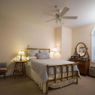 A cozy bedroom with vintage decor, including a bed, dresser with mirror, and a comfortable armchair by the window.