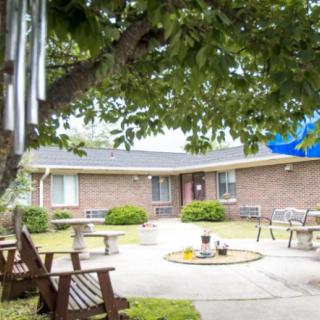 A peaceful courtyard featuring a brick building with outdoor benches and tables under the trees.