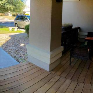 A cozy porch with wooden decking and chairs, overlooking a driveway with a parked car.