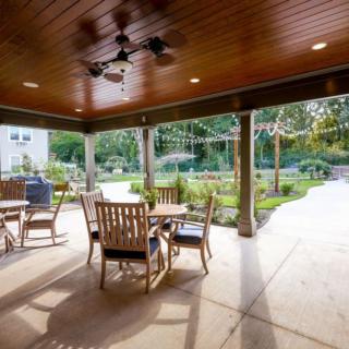 A covered patio with wooden furniture overlooking a garden.
