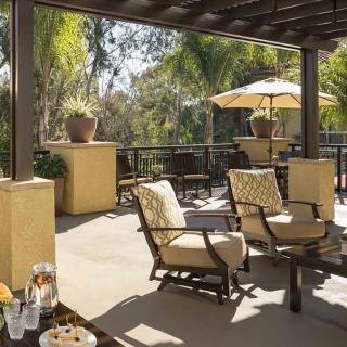 A sunny patio with comfortable outdoor seating and an umbrella, surrounded by lush trees.