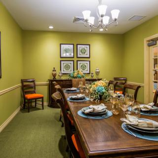 A well-decorated dining room with a large wooden table, elegant place settings, and decorative artwork on green walls.
