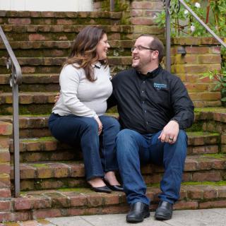 A couple sitting on outdoor brick stairs, smiling at each other.