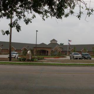 A view of a healthcare facility from the street, featuring a landscaped entrance and parked vehicles.