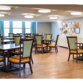 A spacious dining room featuring multiple tables and chairs, with wood flooring and decorative wall art.