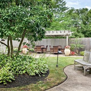 A serene backyard garden with lush greenery, a pergola, and outdoor seating area.