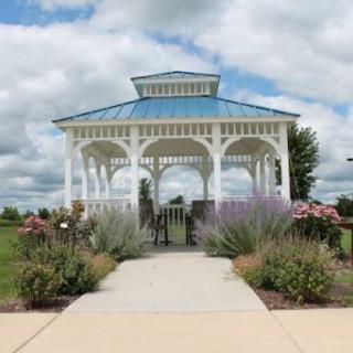 A charming gazebo surrounded by vibrant flowers and a well-maintained pathway, set against a cloudy sky.