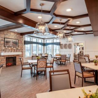 A modern dining room interior with elegant furniture and lighting, featuring large windows and a stone fireplace.